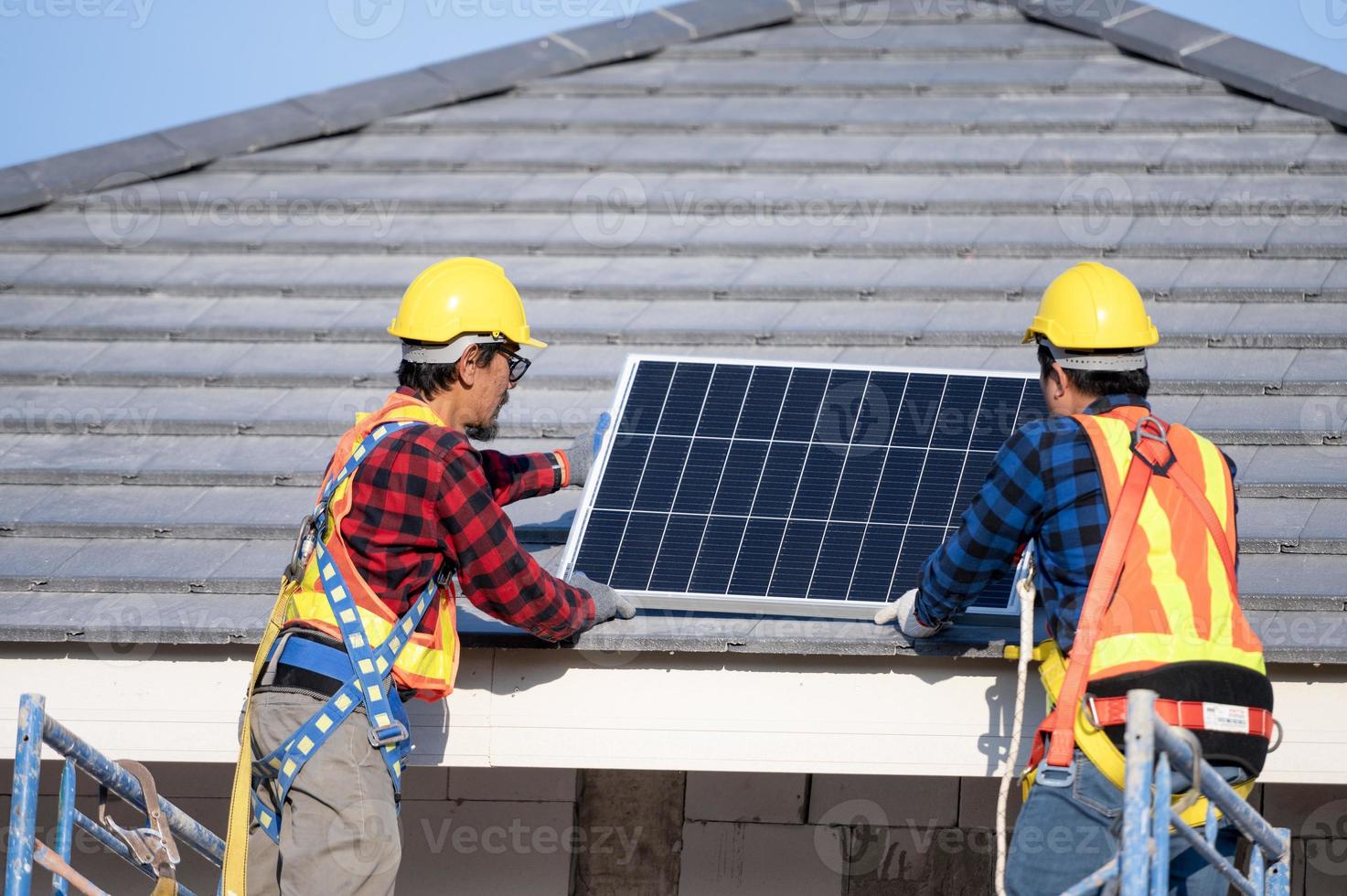 en team av asiatisk tekniker installerar sol- paneler på de tak av en hus. tvärsnitt se av byggare i hjälm montera sol- panel systemet begrepp av förnybar energi foto