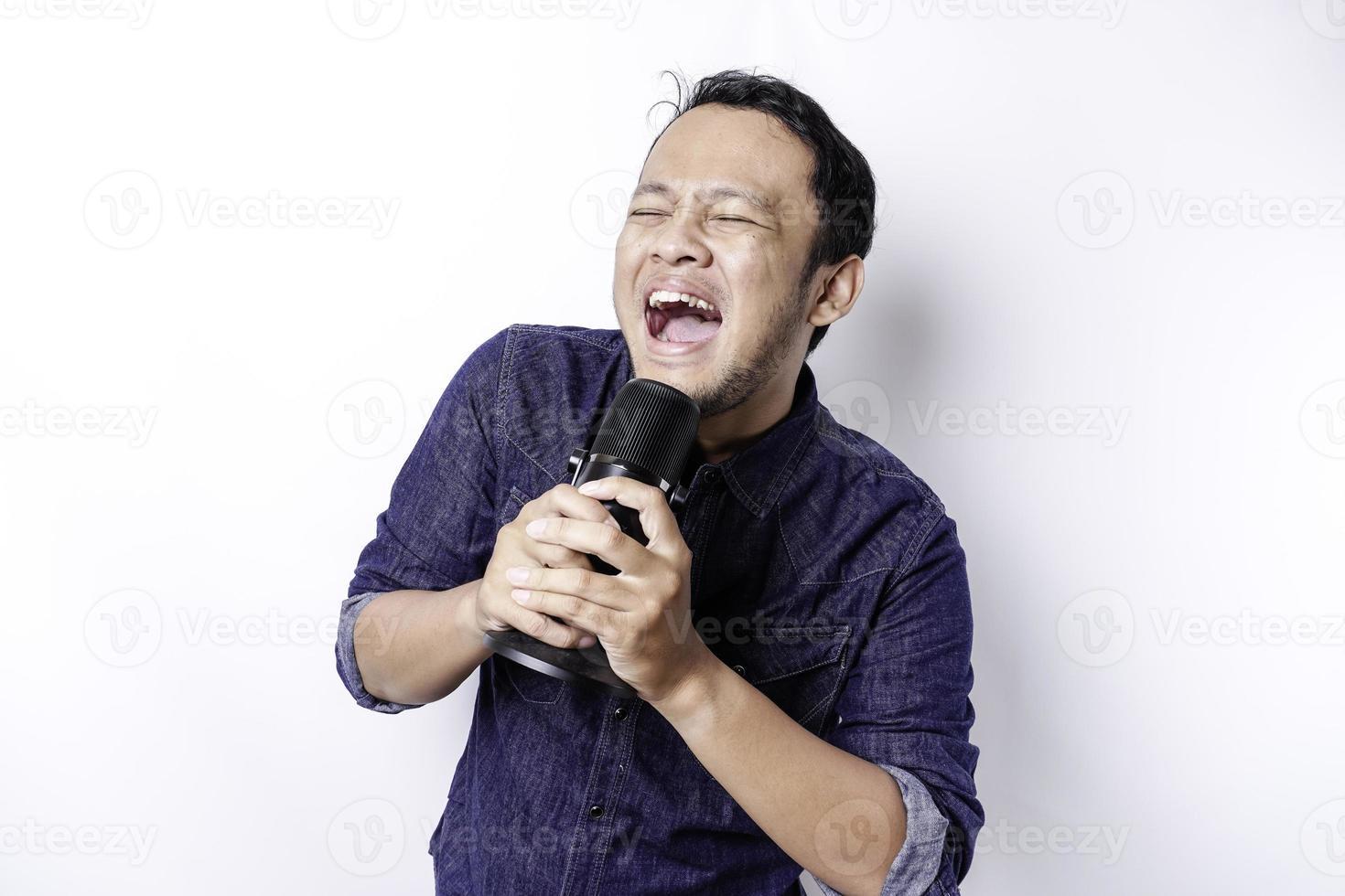 porträtt av sorglös asiatisk man, har roligt karaoke, sång i mikrofon medan stående över vit bakgrund foto