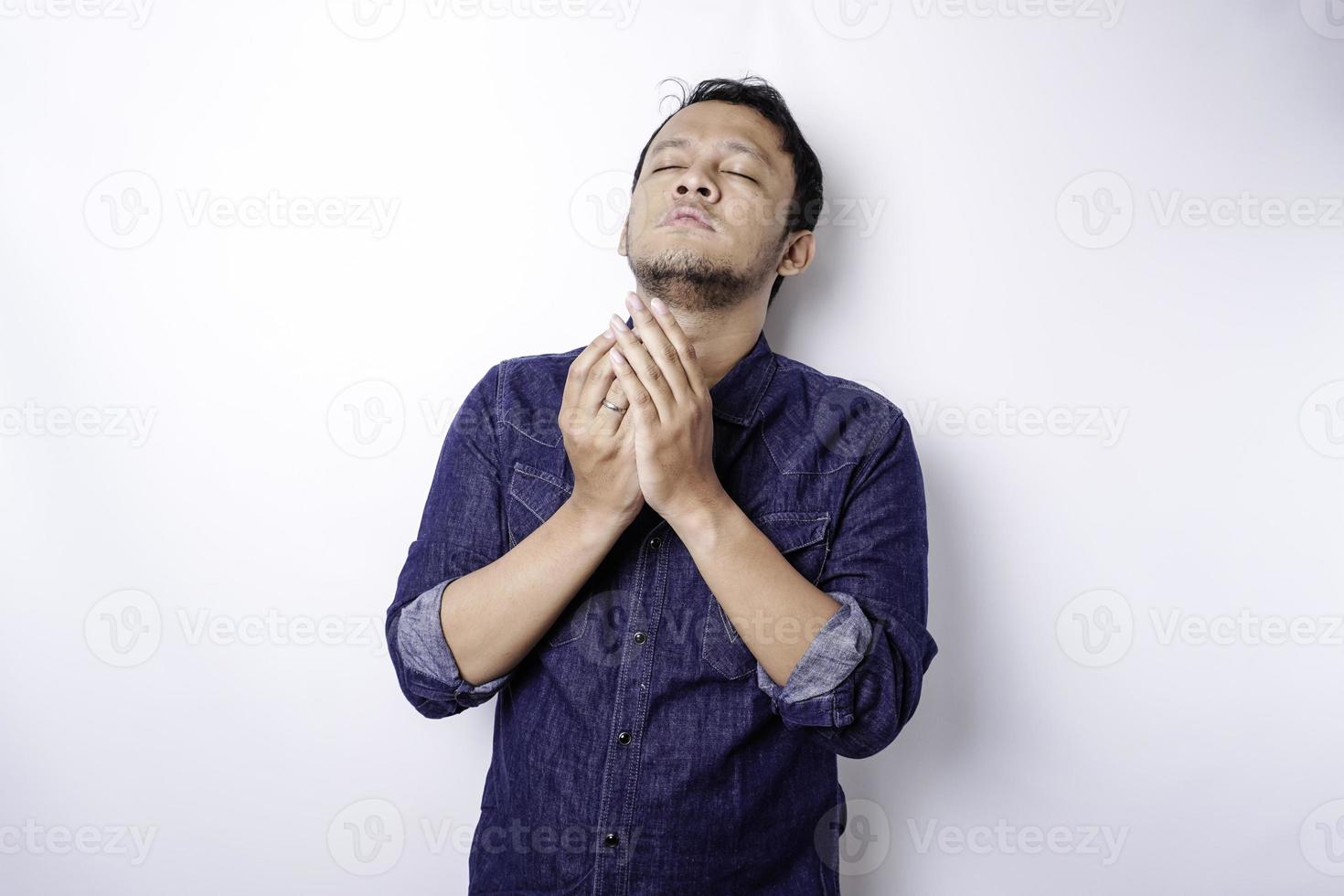 lugn andlig stilig asiatisk kille som ber med slutna ögon. allvarlig fredlig ung man med att förena händer mediterar. tro koncept foto