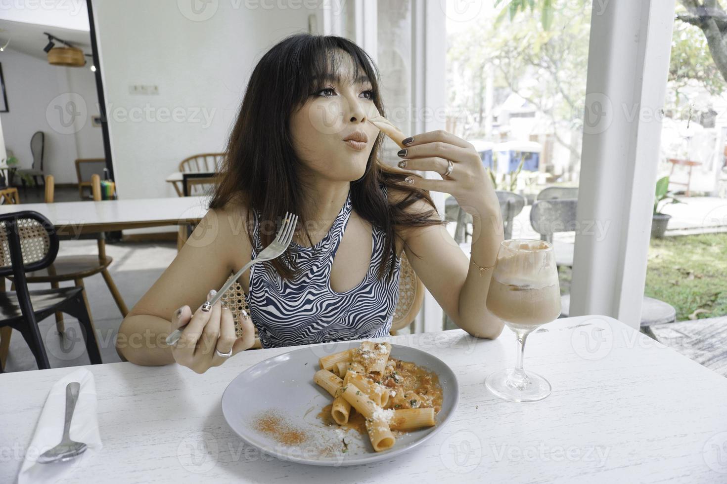 rolig ung asiatisk kvinna äter gott pasta i Kafé foto