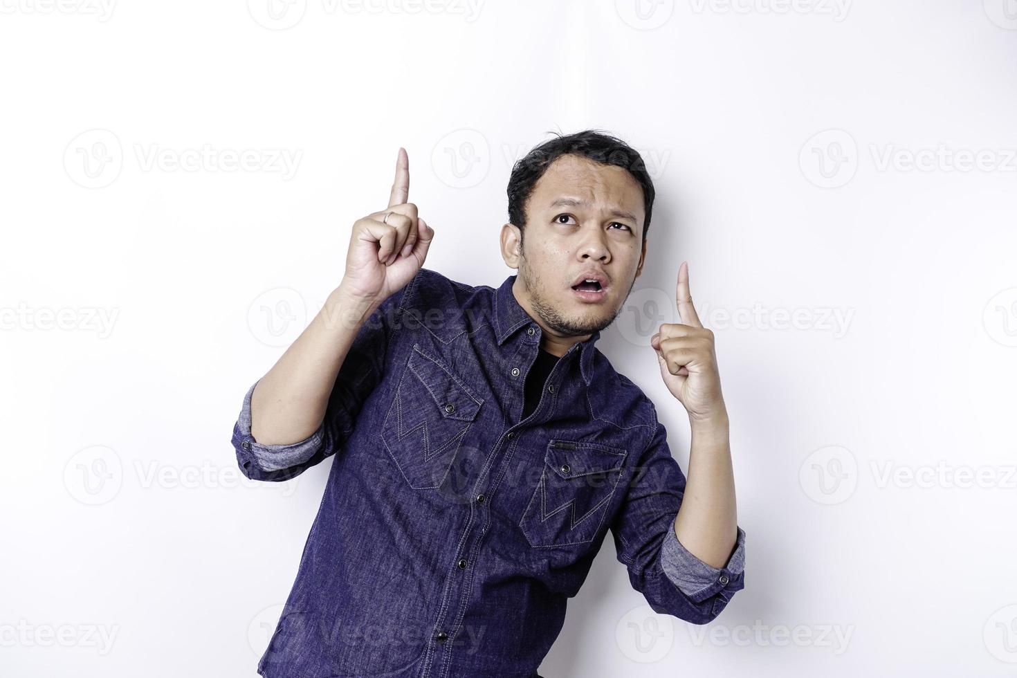 chockade asiatisk man bär blå skjorta pekande på de kopia Plats på topp av honom, isolerat förbi vit bakgrund foto