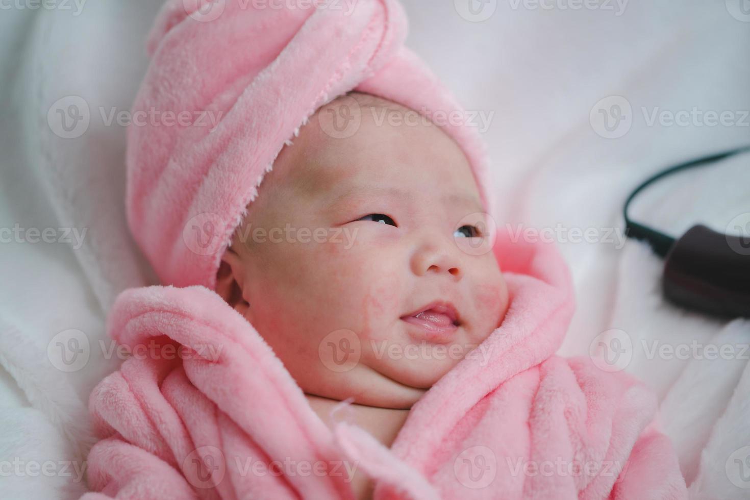 närbild söt nyfödd bebis i rosa kroppsdräkt liggande ner ensam på säng. förtjusande spädbarn vilar på vit lakan, stirrande på kamera ser fredlig. barndom, sjukvård och pediatrik, barndom begrepp foto