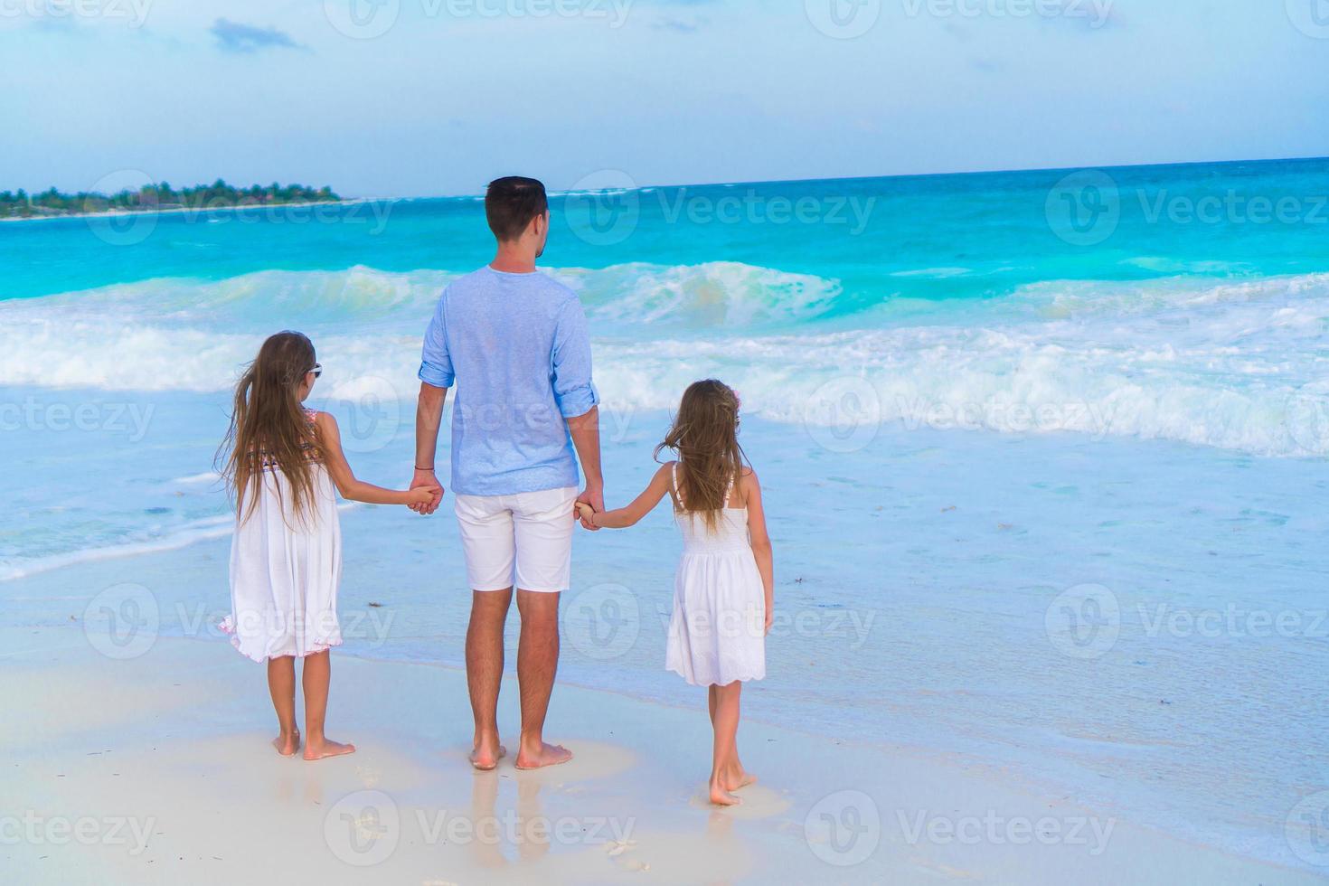 familj av pappa och barn gående på vit tropisk strand på karibiska ö foto