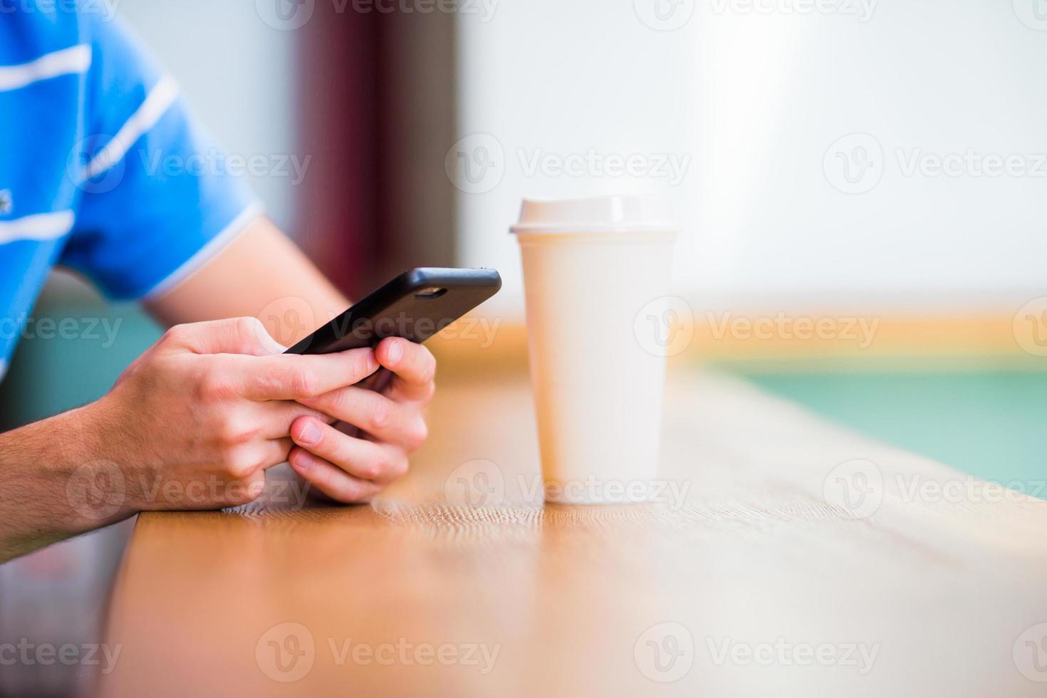 närbild av manlig händer innehav mobiltelefon och klass av Coffee i Kafé. man använder sig av mobil smartphone foto