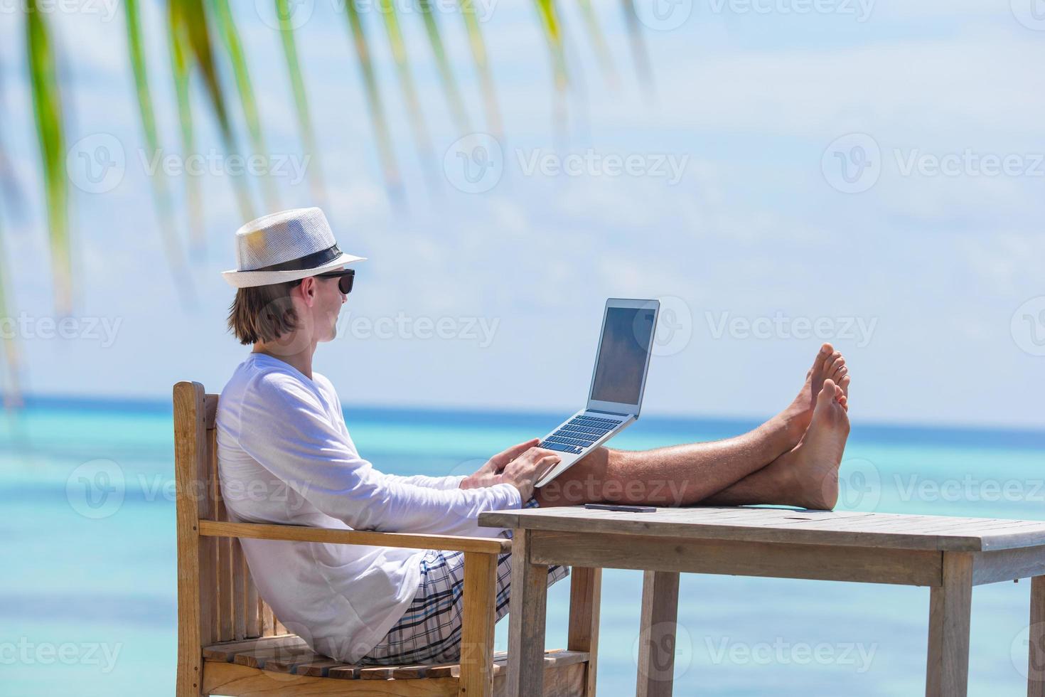 ung man med läsplatta dator under tropisk strand semester foto