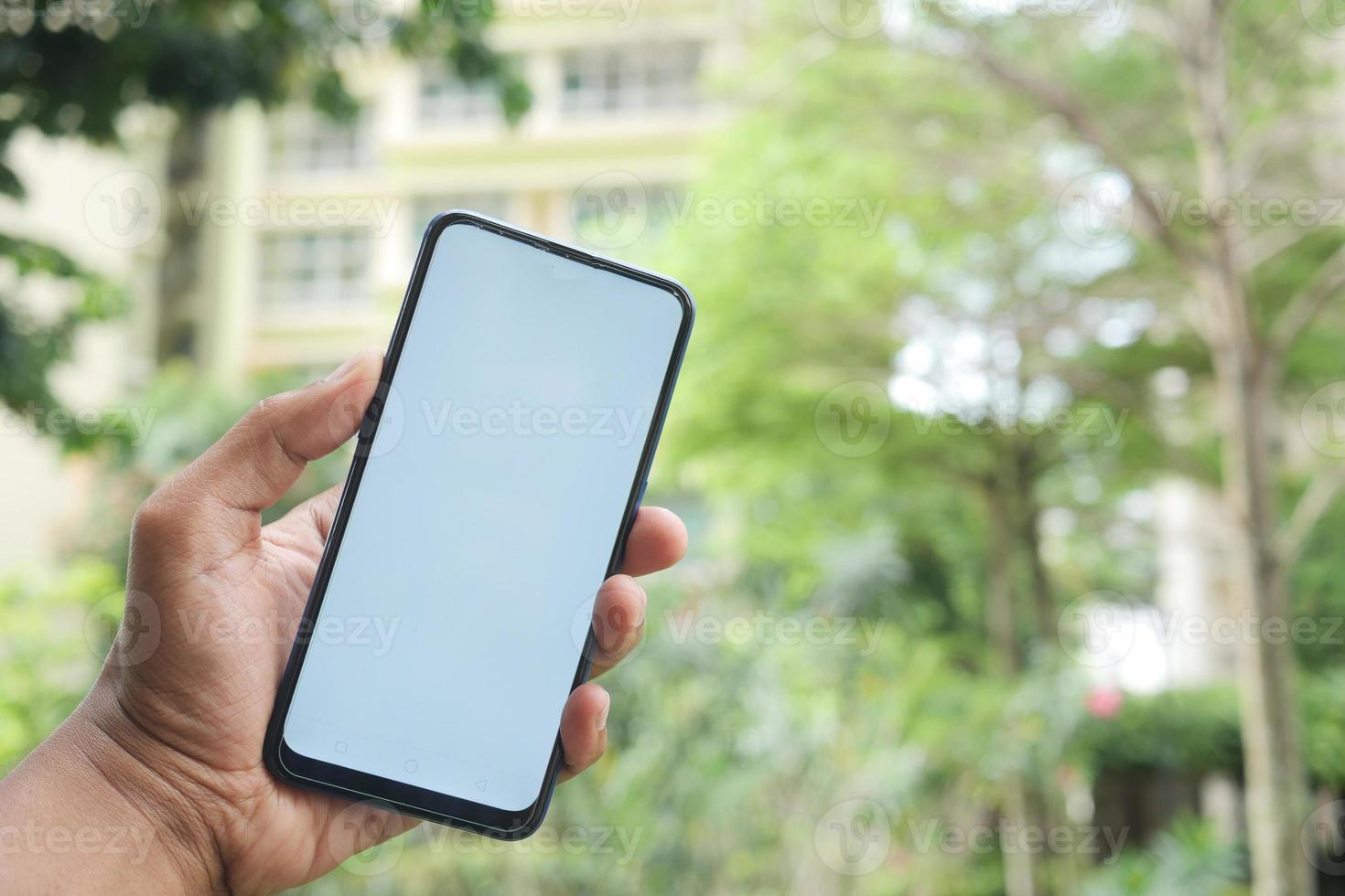 ung man hand använder sig av smart telefon med grön skärm mot stad byggnader foto