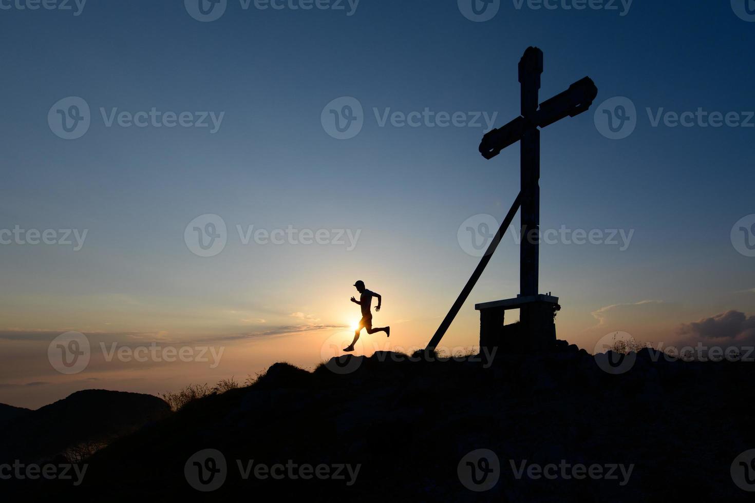 silhuett av man löpning i de miljö Sol på topp av en berg med de korsa foto