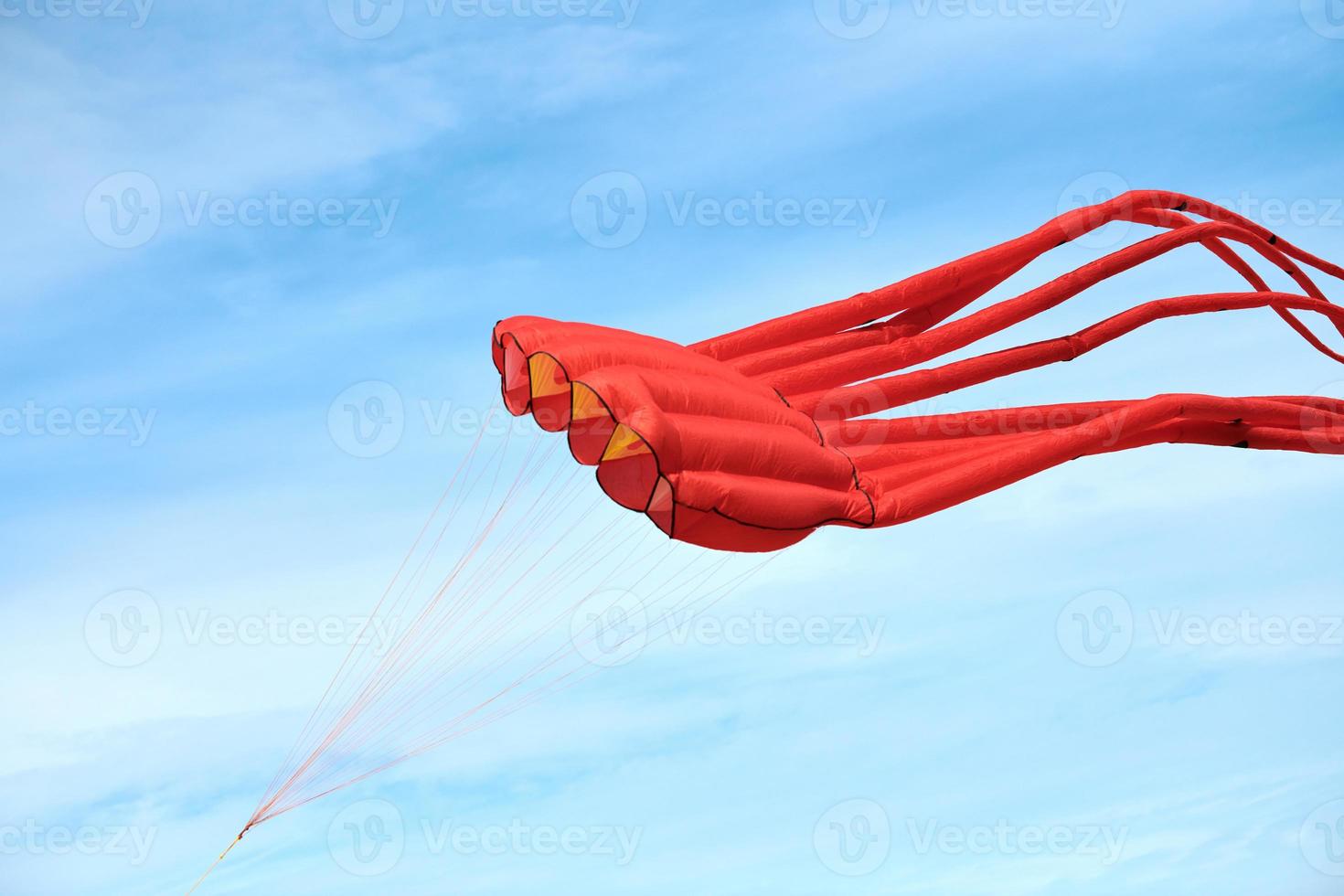 ljusröd rosa bläckfiskdrake som flyger på blå himmel med moln, röd bläckfiskformad drake, drakfestival foto
