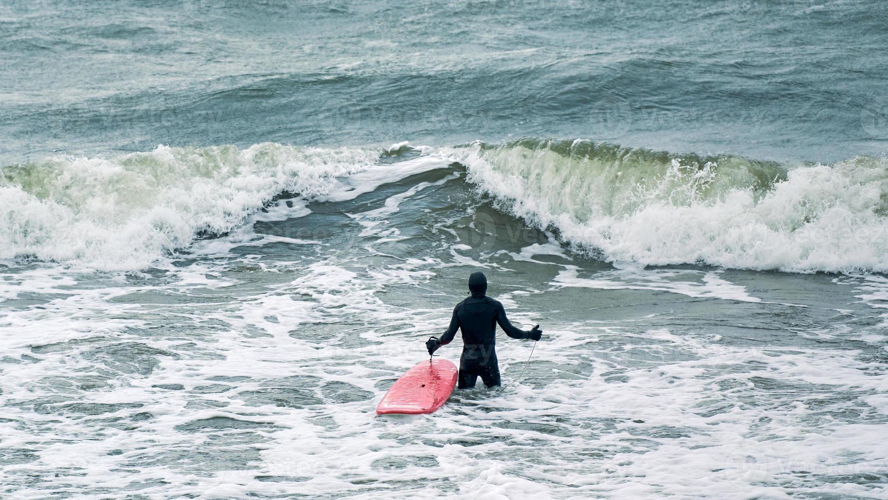 manlig surfare i baddräkt i havet med röd surfbräda foto