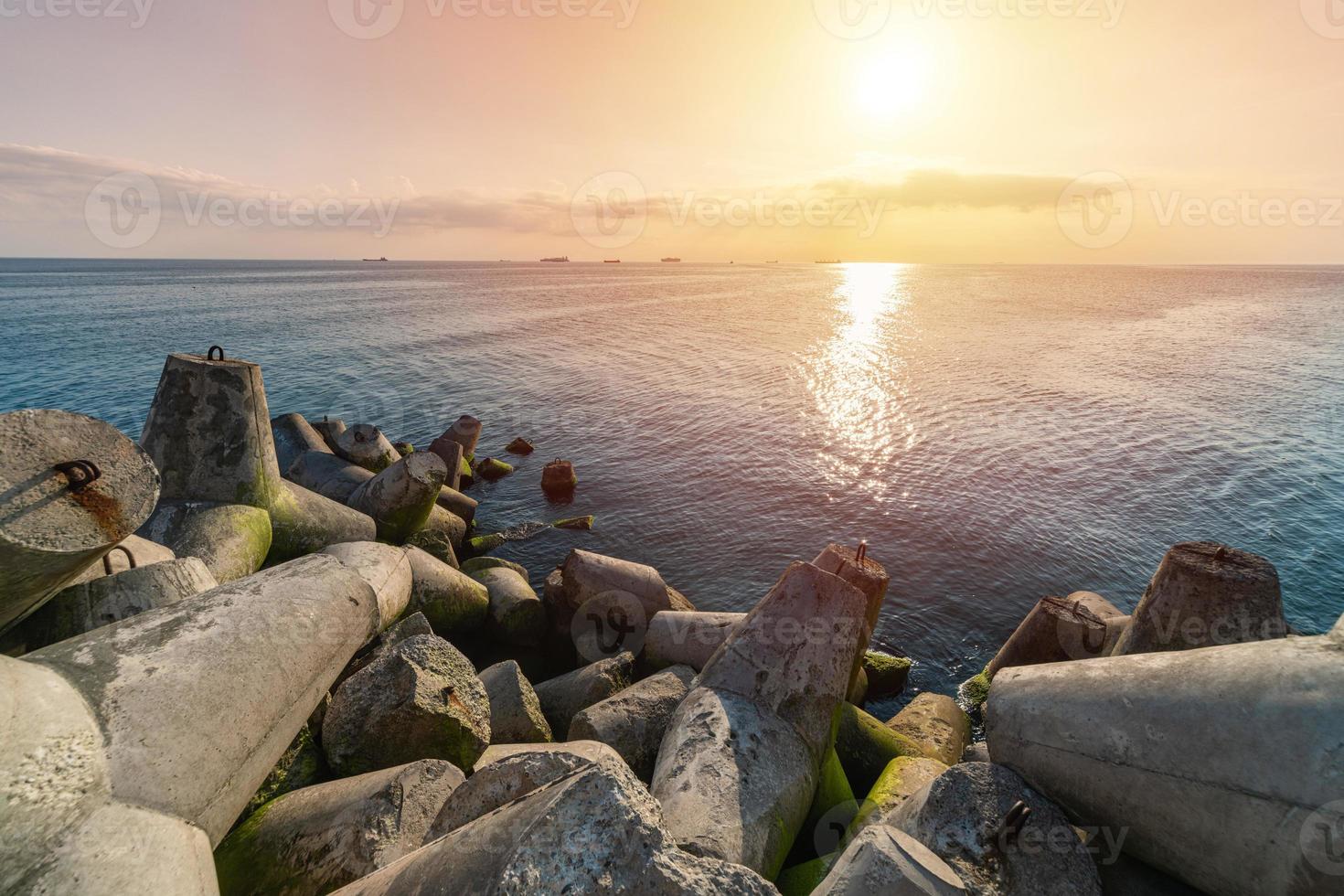 vacker solnedgång havslandskap. vågbrytare tetrapods i land vid piren. lastfartyg vid horisonten. resedrömmar och motivation foto