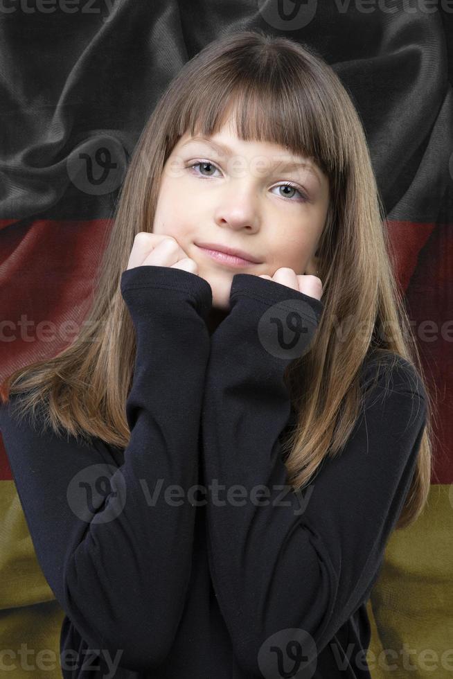 en skön liten flicka med en ljuv leende, stående mot de bakgrund av en suddig flagga av Tyskland. foto