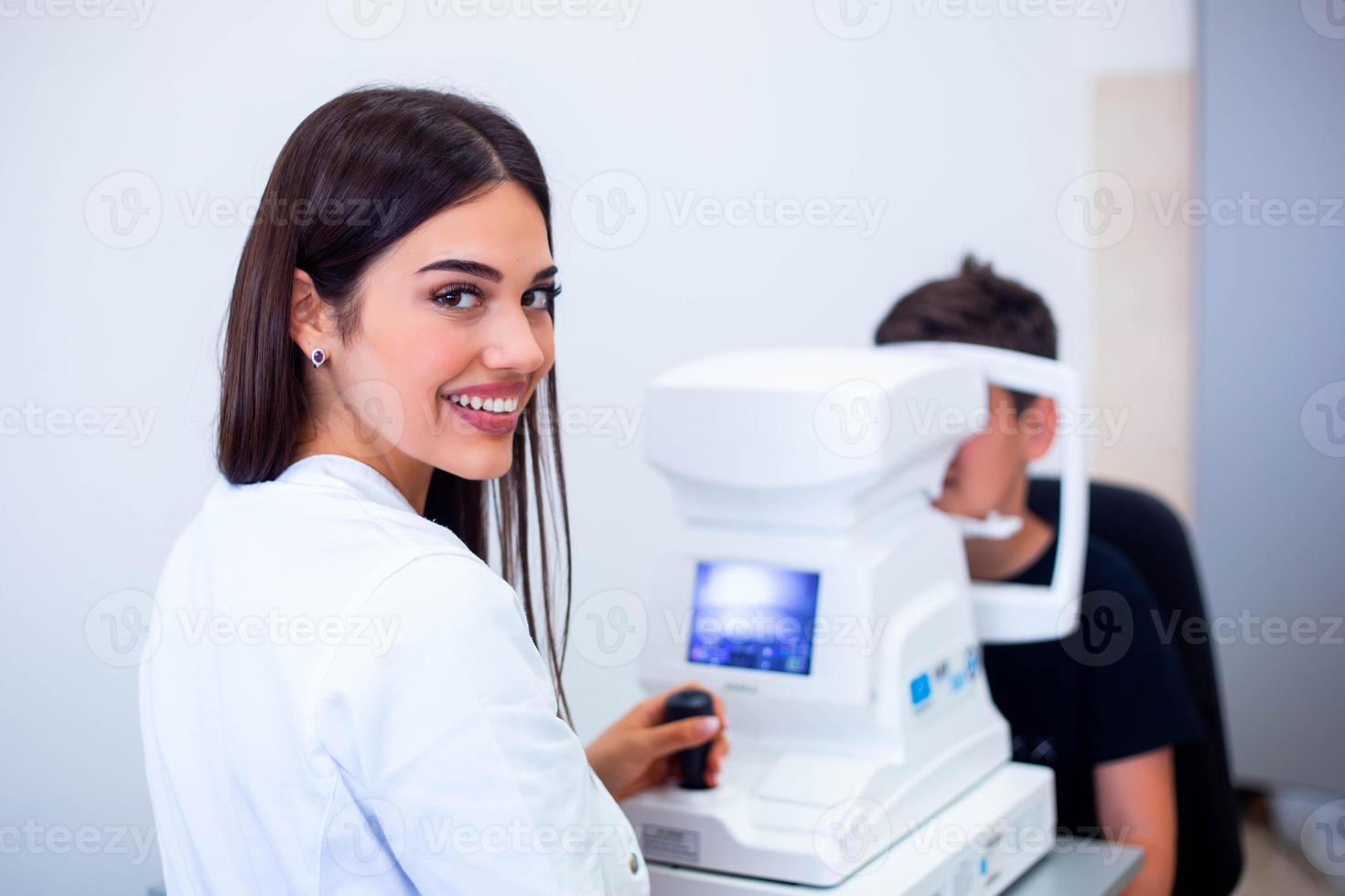 kvinna ögonläkare använder sig av maskin för kontroll öga syn i klinik. liten pojke ser på Utrustning och läkare testning öga elev i optisk Lagra. begrepp av öga vård och hälsa. foto