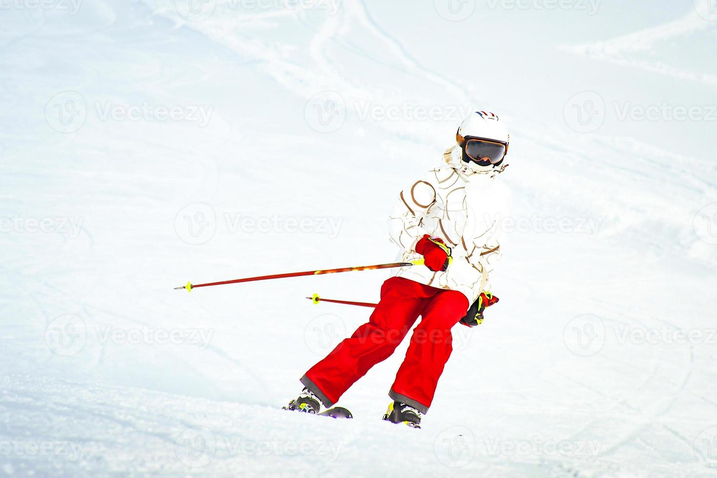 alpina åka skidor. skidåkning kvinna skidåkare gående utför mot snö täckt isolerat vit åka skidor spår backe pist i vinter. Bra rekreations kvinna skidåkare i vit åka skidor jacka och röd byxor foto