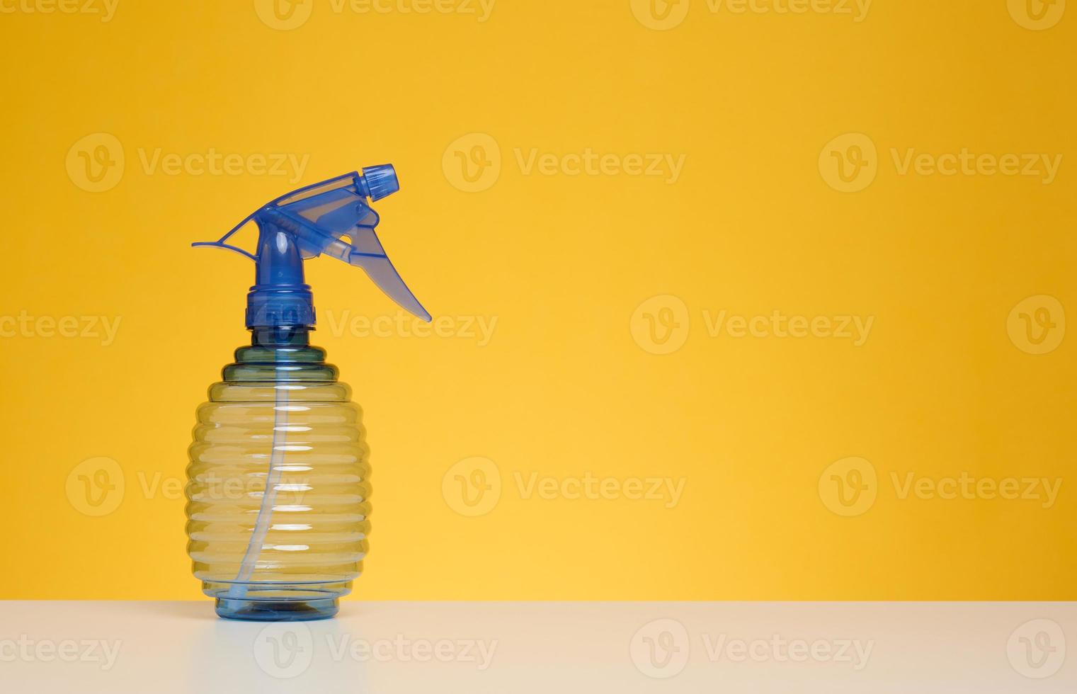 plast flaska med spray för strykning kläder, vattning växter på en vit tabell, gul bakgrund foto