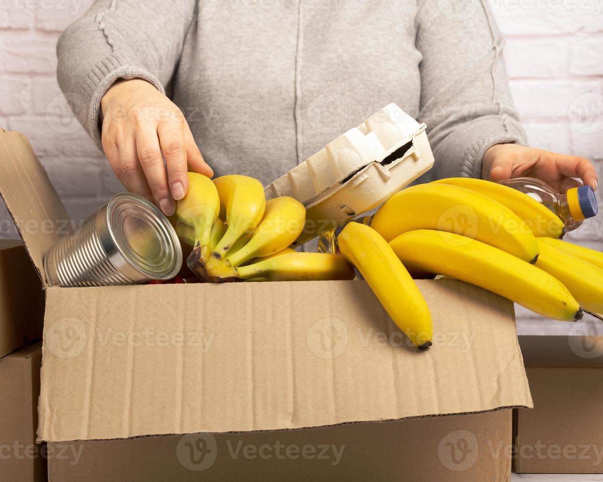 kvinna samlar mat, frukt och saker i en kartong låda till hjälp de där i behöver, hjälp och volontär begrepp foto