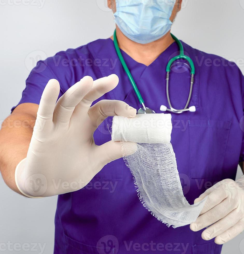 läkare i blå enhetlig och latex handskar innehav vit steril flor klä på sig bandage foto