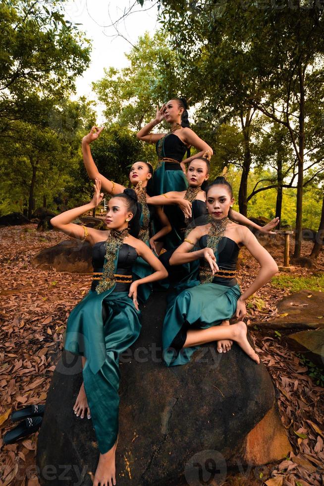 en grupp av asiatisk människor i grön kostymer Sammanträde på en stor sten med brun löv i de bakgrund foto