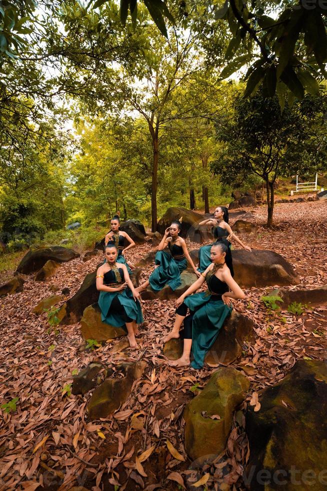 en grupp av indonesiska dansare Sammanträde underbart på de sten med brun löv i de bakgrund inuti de skog foto