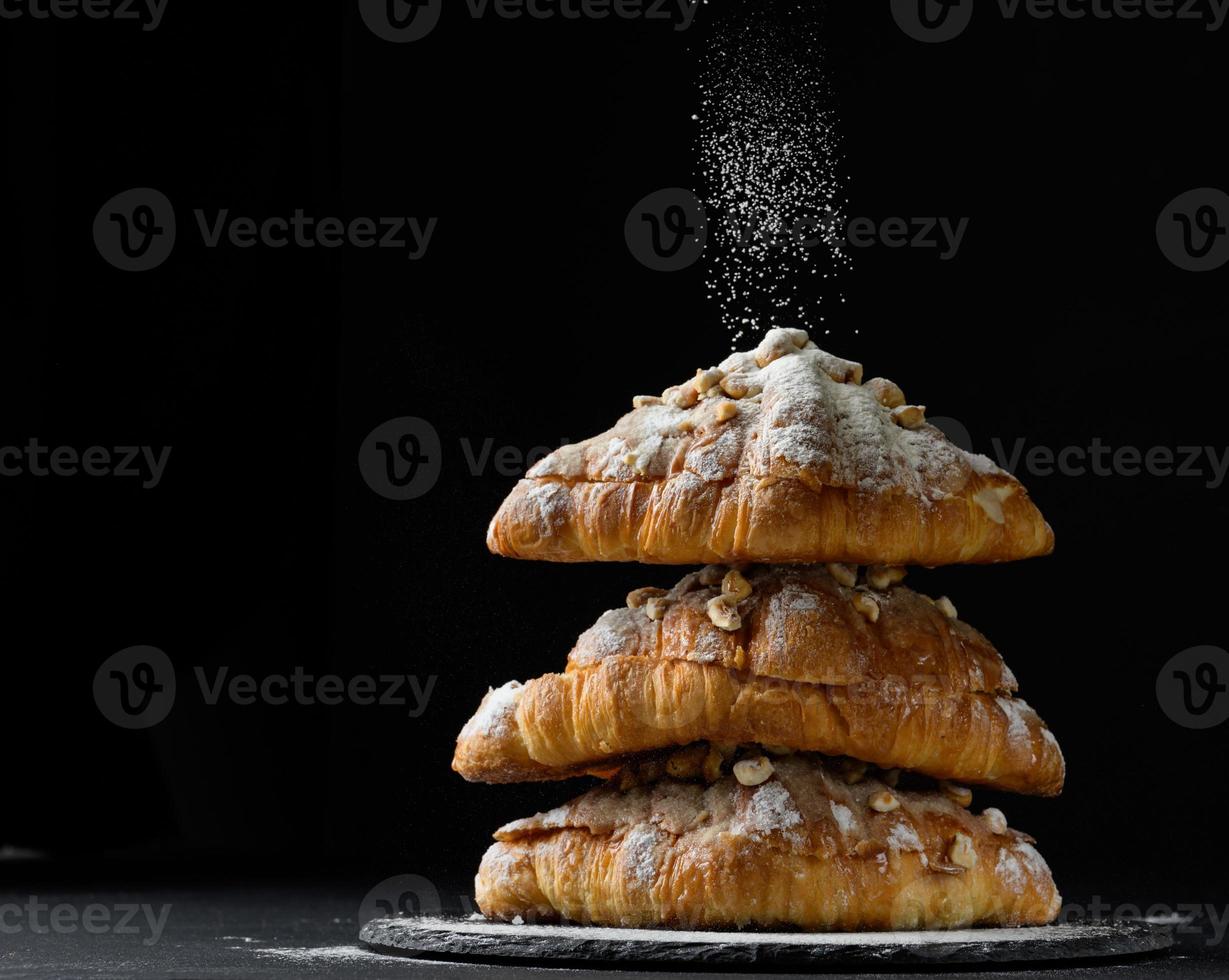 en stack av bakad croissanter stänkte med pulveriserad socker på en svart bakgrund foto