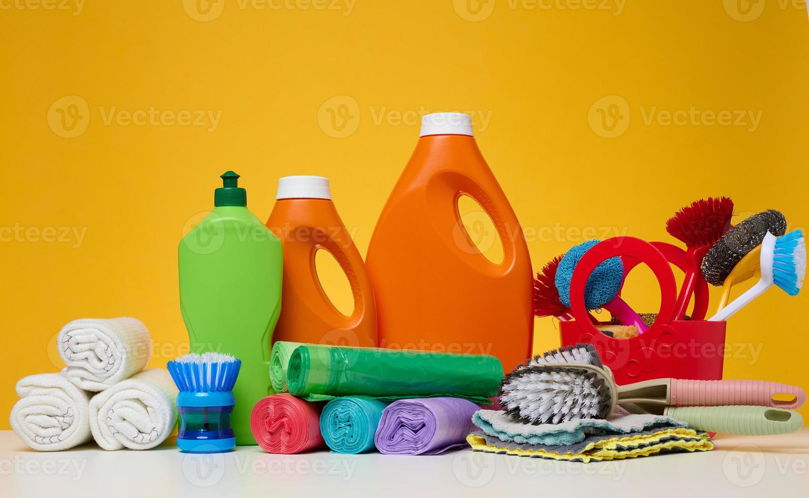 orange plast flaskor med flytande Produkter och sopor påsar, borstar och textil- trasor för tvättning golv på en vit tabell foto