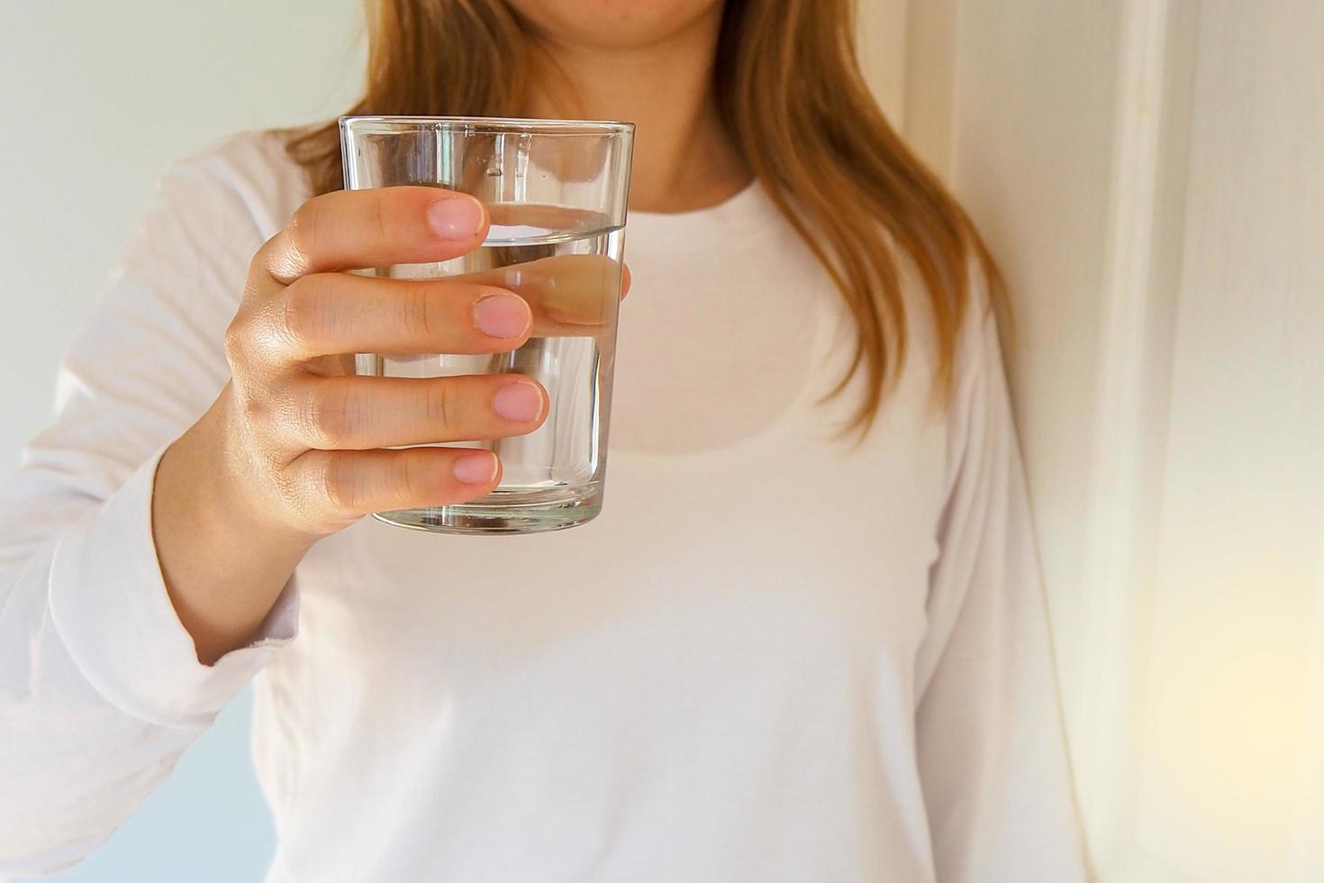en kvinna innehav en glas av vatten till dryck. dricka vatten är välgörande till de kropp. Bra hälsa begrepp foto