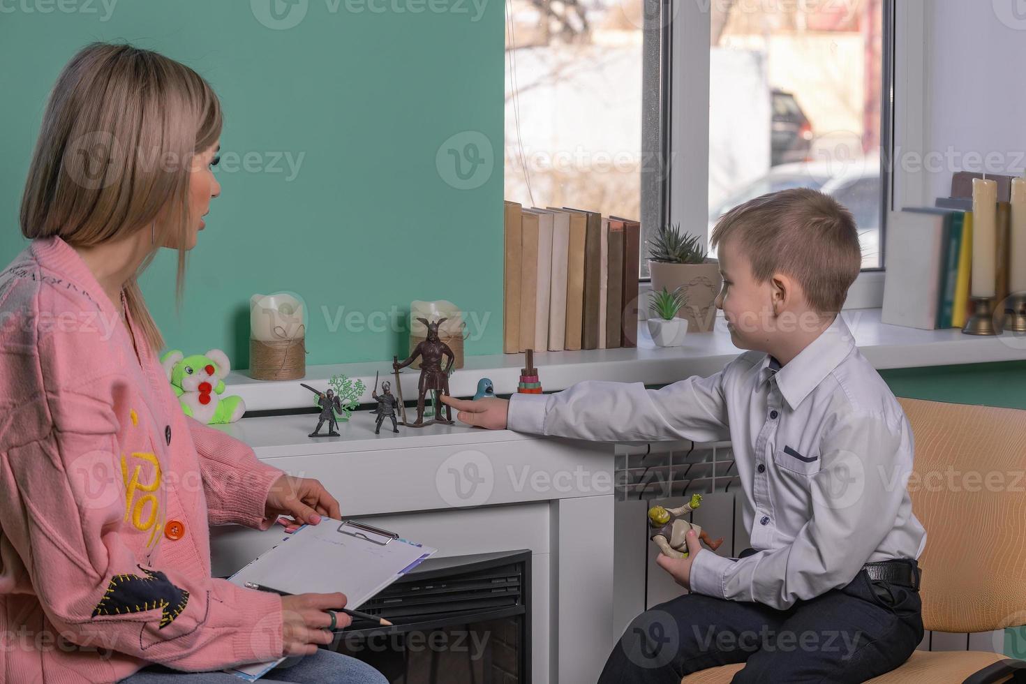 en skön kvinna barn psykolog Arbetar i henne kontor med en barn, en pojke av 6-8 år gammal. de psykolog konfidentiellt utför en konversation med de barn med de hjälp av leksaker. foto