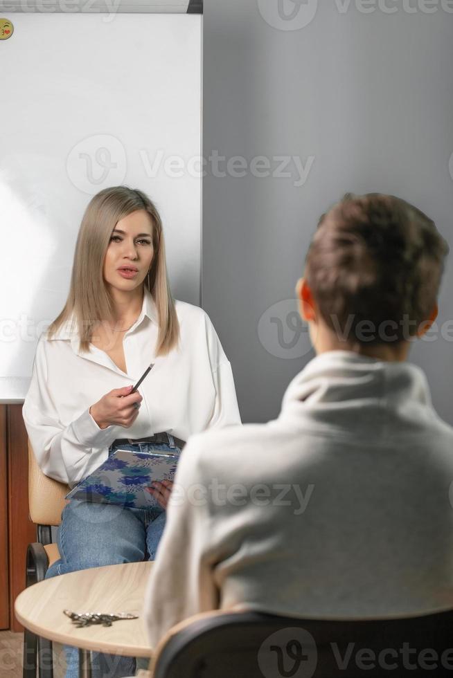 skön kvinna psykolog Arbetar i henne kontor med en ung man klient. i de händer av en psykolog, de anteckningar hon gör under de konversation. foto