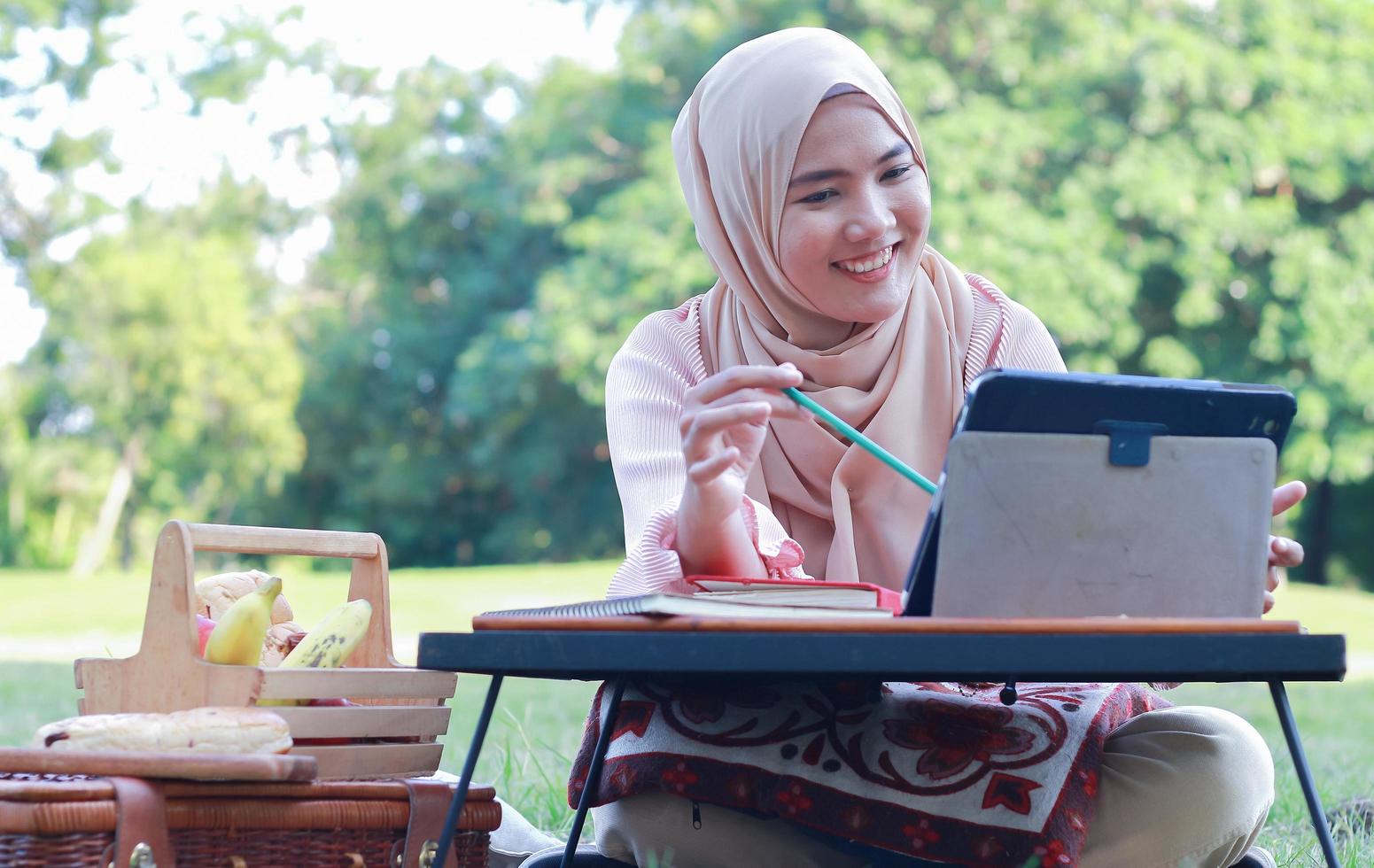 vacker muslimsk flicka sitter lyckligt i parken. muslimsk kvinna som ler i trädgårdsgräsmattan. livsstilskoncept av en självsäker modern kvinna foto