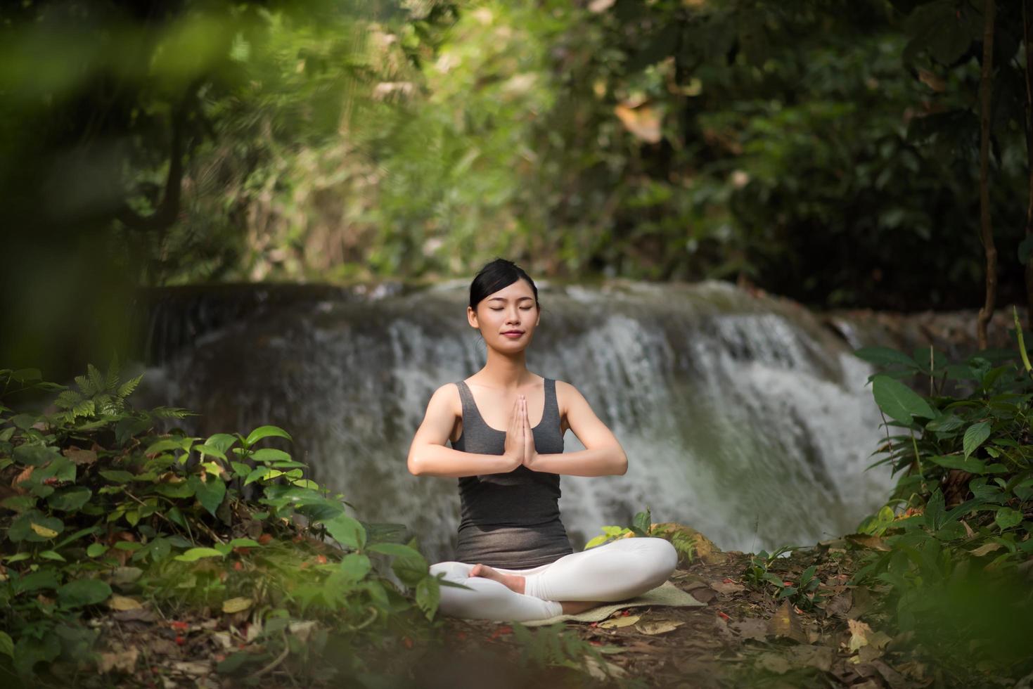 ung kvinna i en yogaställning som sitter nära ett vattenfall foto