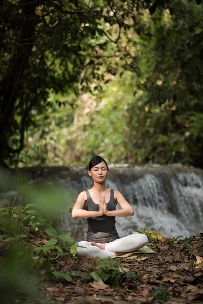 ung kvinna i en yogaställning som sitter nära ett vattenfall foto