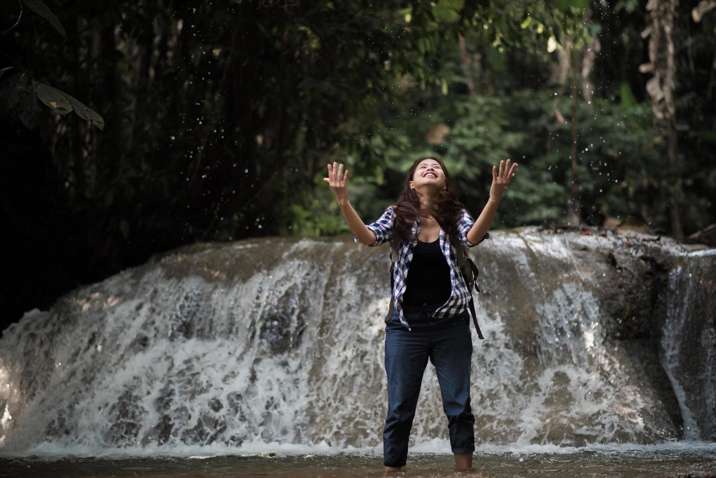 ung kvinna som har kul under ett vattenfall i skogen foto