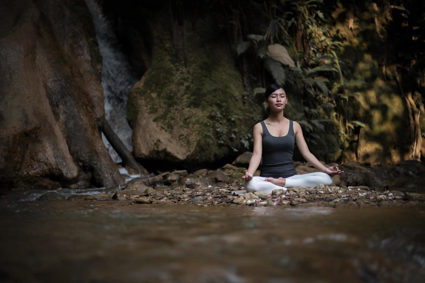 ung kvinna i en yogaställning som sitter nära ett vattenfall foto