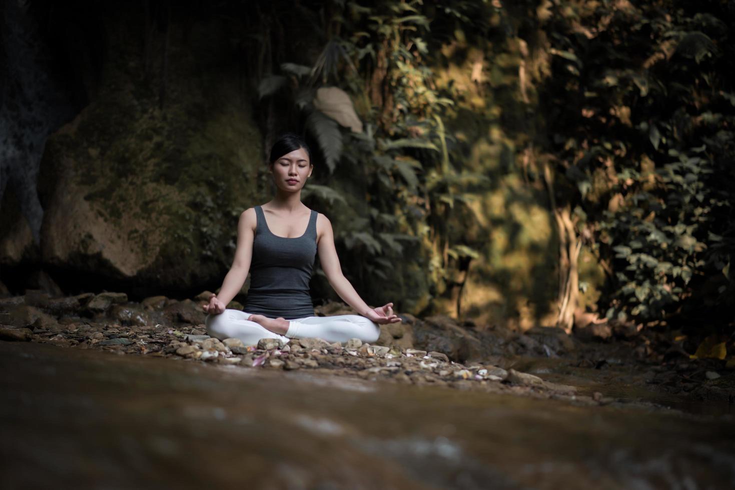 ung kvinna i en yogaställning som sitter nära ett vattenfall foto