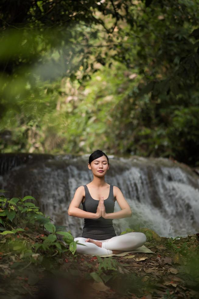 ung kvinna i en yogaställning som sitter nära ett vattenfall foto