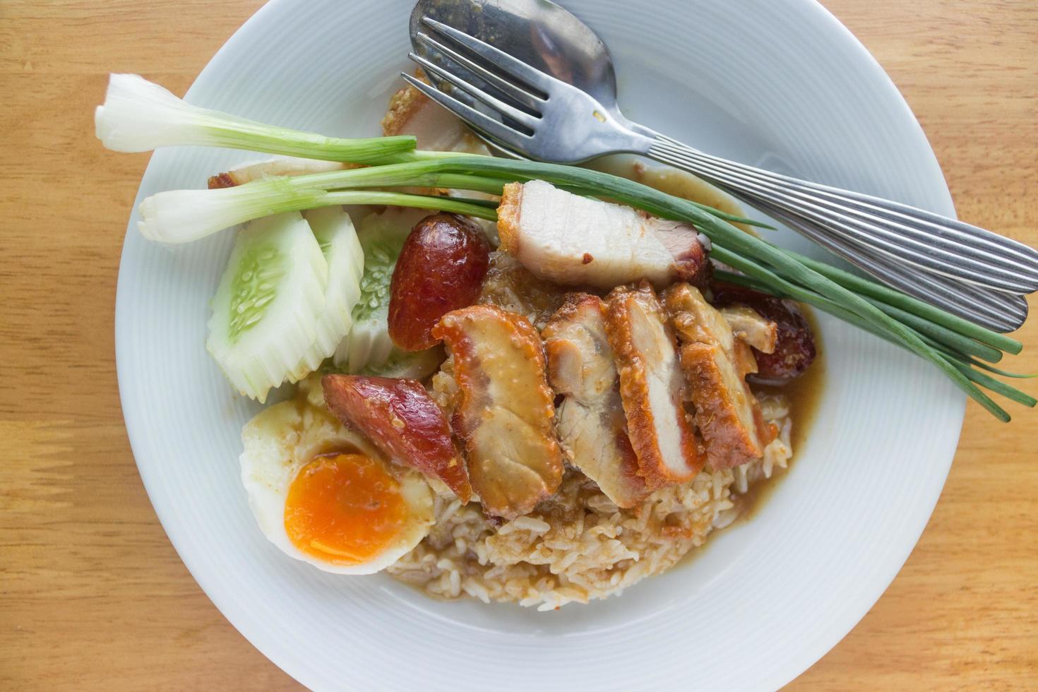 grillat fläsk och skivat kokt ägg med ris och grönsaker på den vita plattan på bordet foto