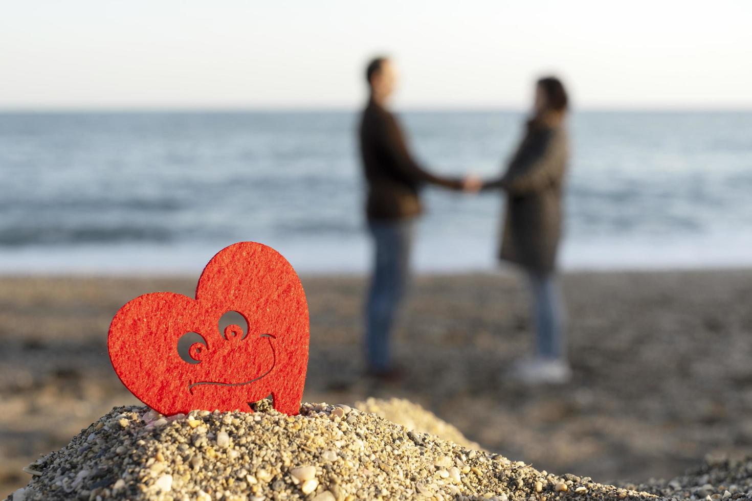 rött hjärta på ett sandberg vid havet med ett par älskare i bakgrunden. begreppet san valentine foto