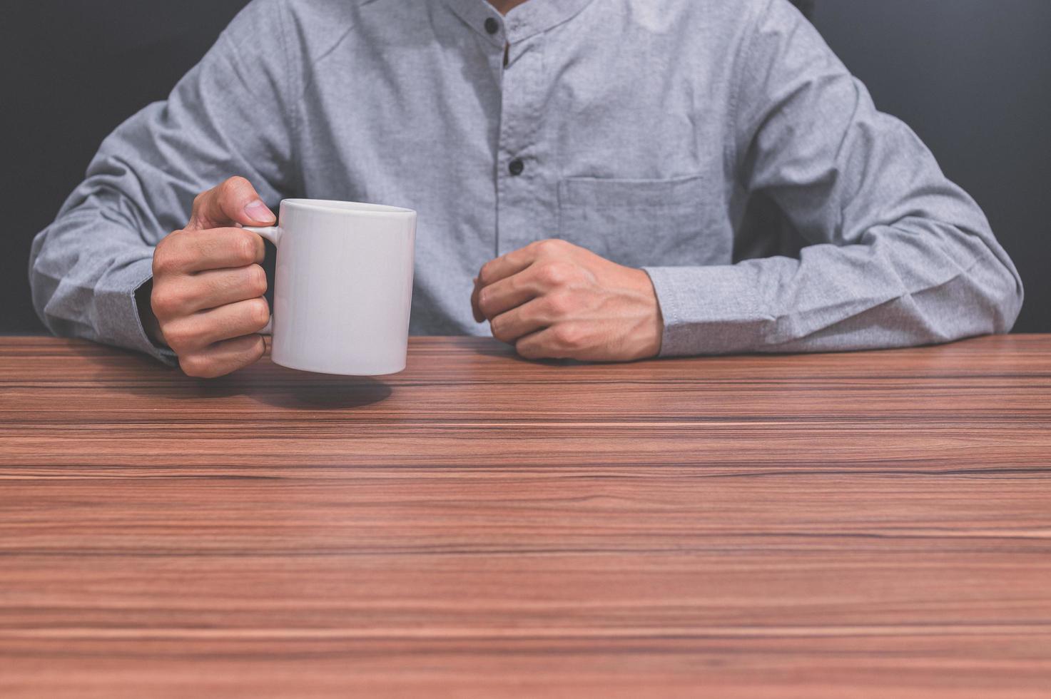 man som håller en kaffekopp vid sitt skrivbord foto