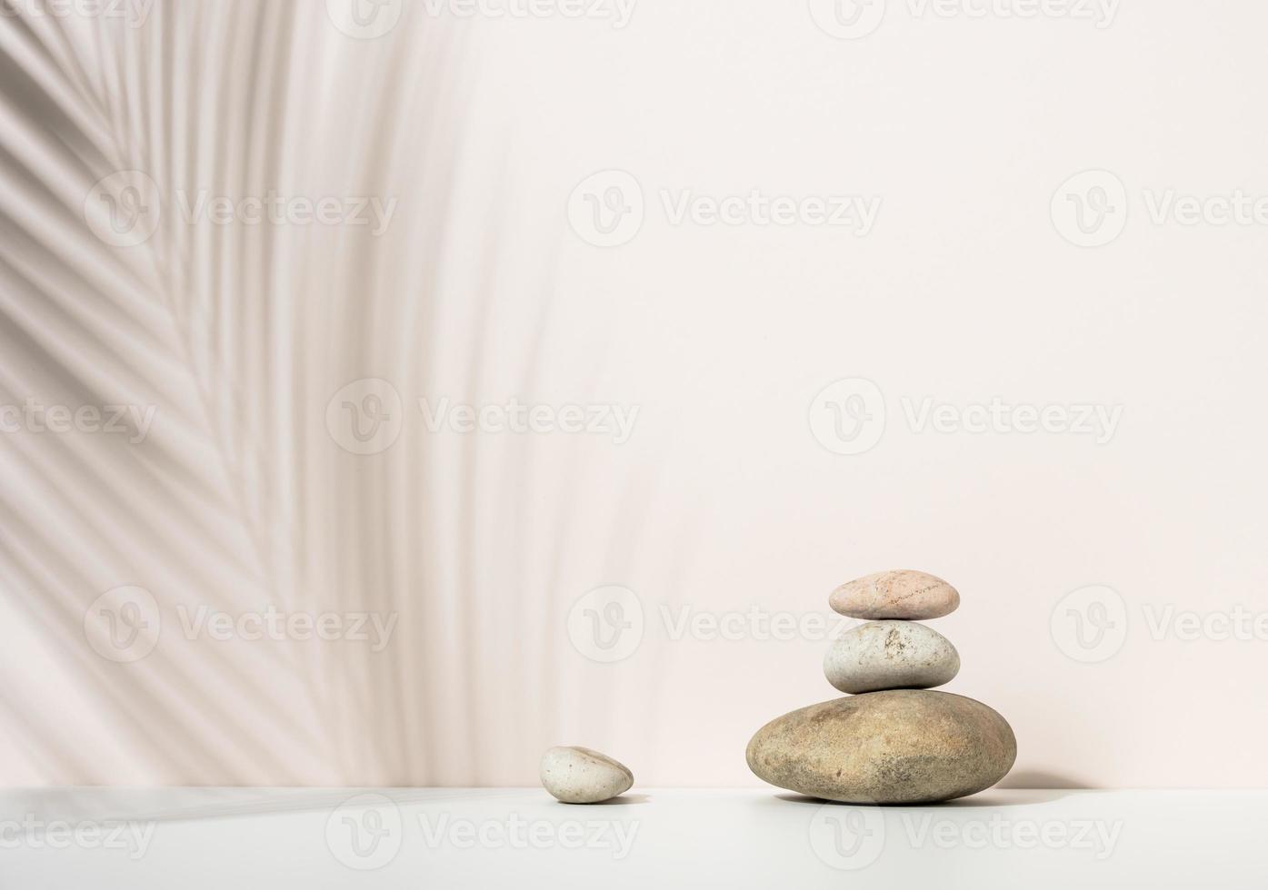 stack av runda stenar och och de skugga av en handflatan blad på en beige bakgrund. scen för demonstration av kosmetisk Produkter, reklam foto