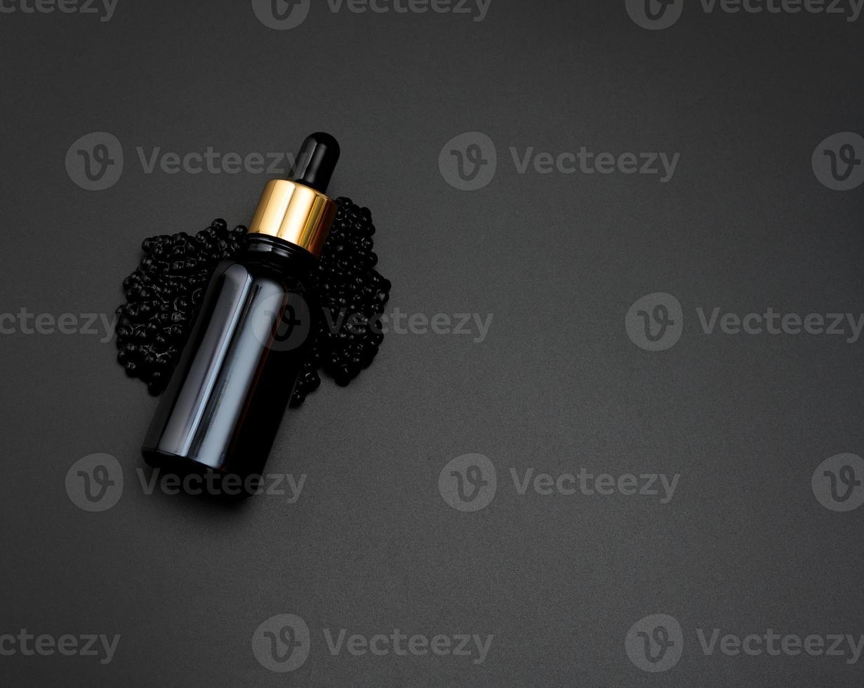 glas flaska med en pipett lögner på en högen av svart kaviar, svart bakgrund. naturlig komisk. produkt branding foto