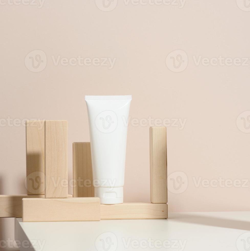 tömma vit plast rör för kosmetika på en beige bakgrund med trä- block. förpackning för grädde, gel, serum, reklam och produkt befordran, falsk upp foto