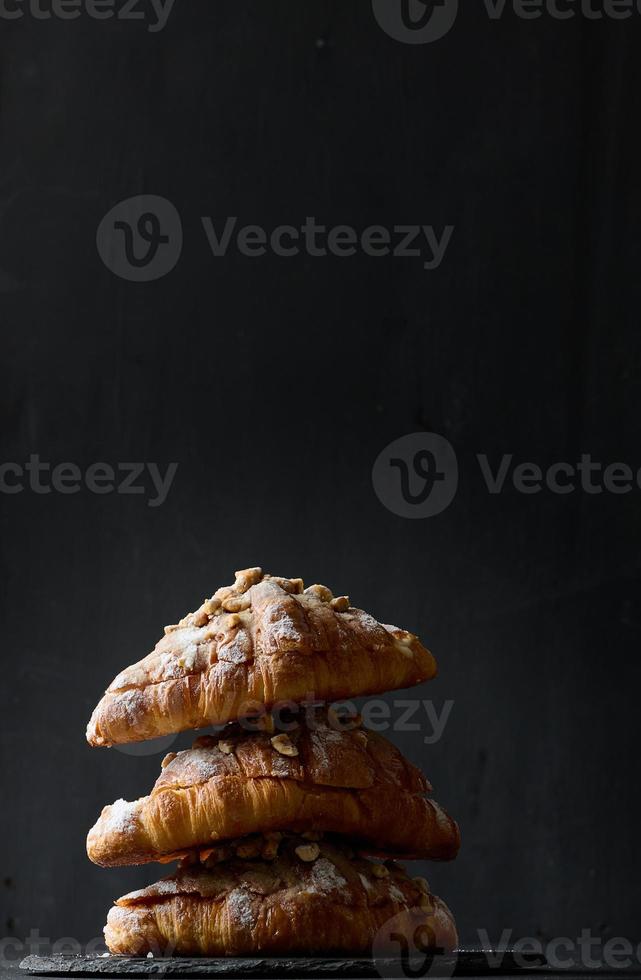 stack av bakad croissanter stänkte med pulveriserad socker på en svart bakgrund foto