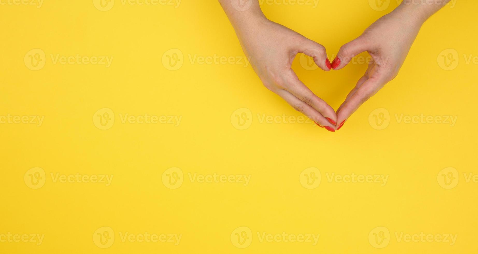 två kvinna händer vikta i de form av en hjärta på en gul bakgrund. tacksamhet och vänlighet begrepp, baner foto