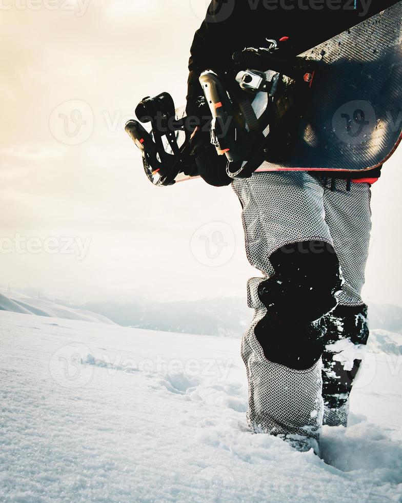 snowboardåkare klädd i en full skyddande redskap för extrem snålskjuts åka snowboard Framställ med en snowboard gående. isolerat på grå vit snö bakgrund. foto