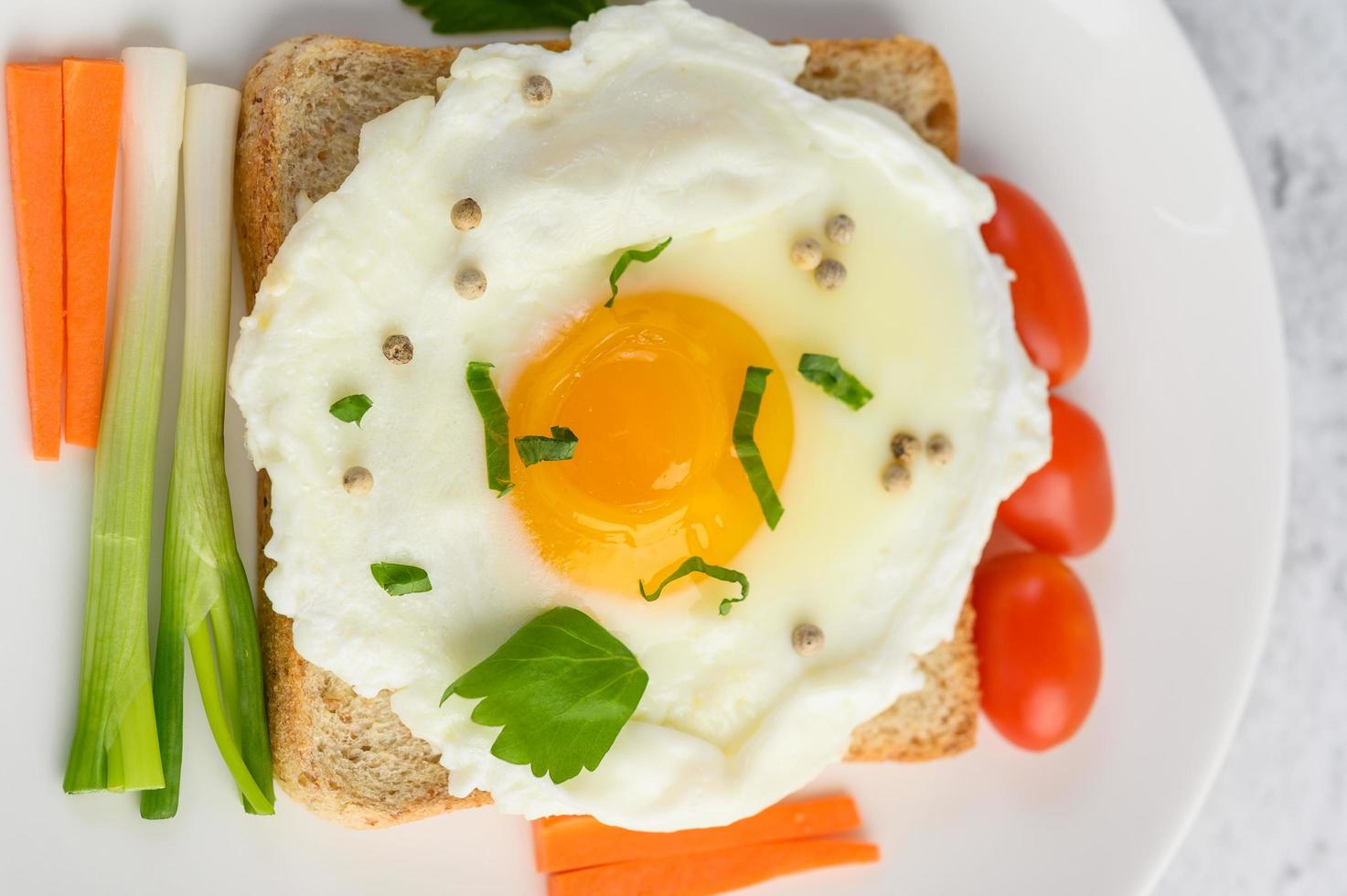 ett stekt ägg på toast toppat med pepparkärnor med morötter och vårlök foto