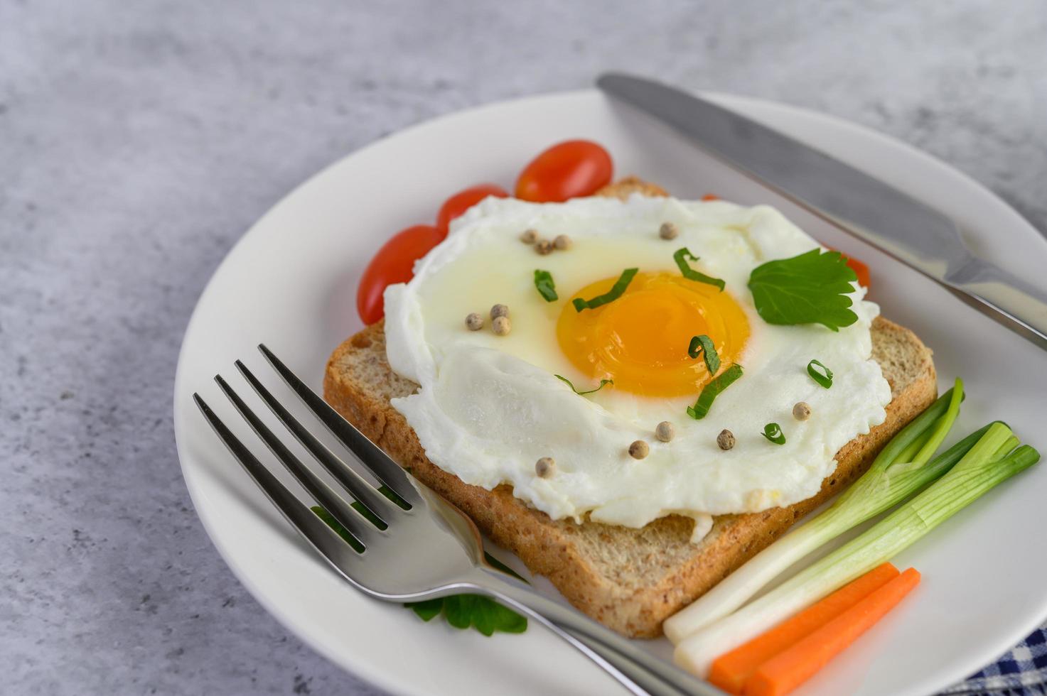 ett stekt ägg på toast toppat med pepparkärnor med morötter och vårlök foto