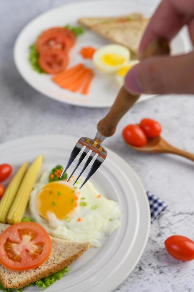 gaffel som når friterade ägg med bröd med grönsaker till frukost foto