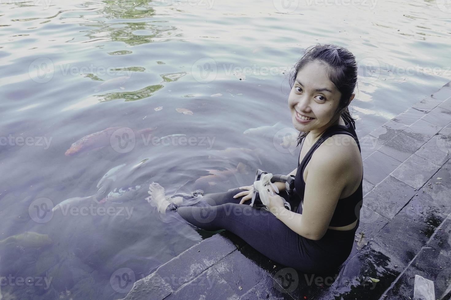 attraktiv ung kvinna Sammanträde förbi de kant av en simning slå samman, innehav en Google foto