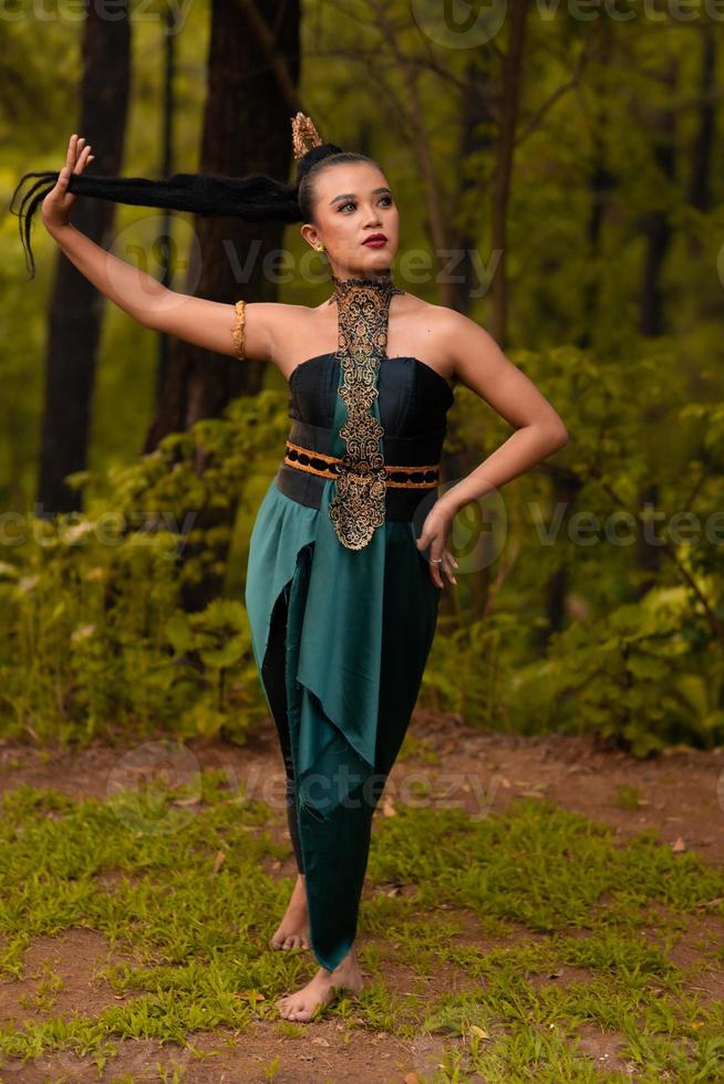 skön asiatisk kvinna innehav henne svart hår medan stående i främre av de skog i en grön kostym foto