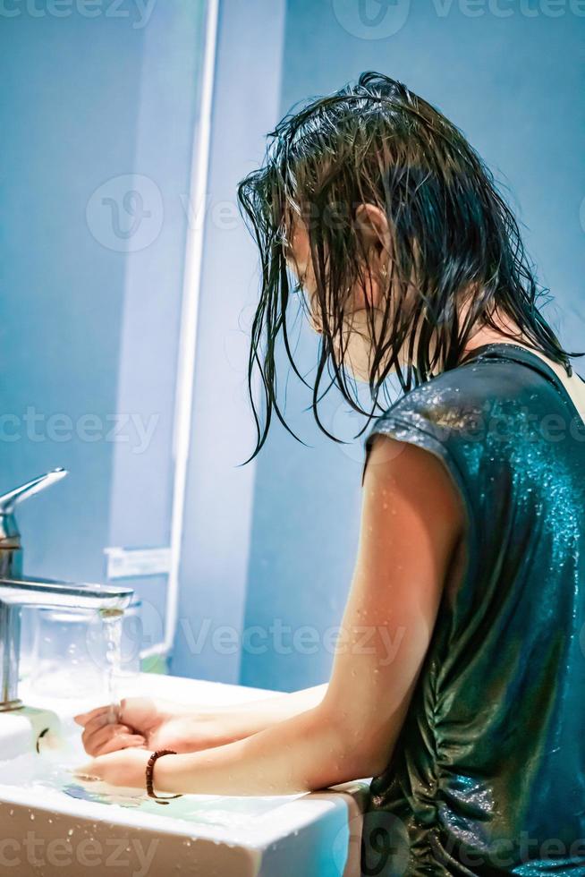 en ung kvinna tvättar henne händer i de vit handfat från de virus covid-19 foto