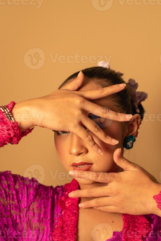 porträtt av balinesisk kvinna med rosa klänning utgör med händer på de ansikte foto